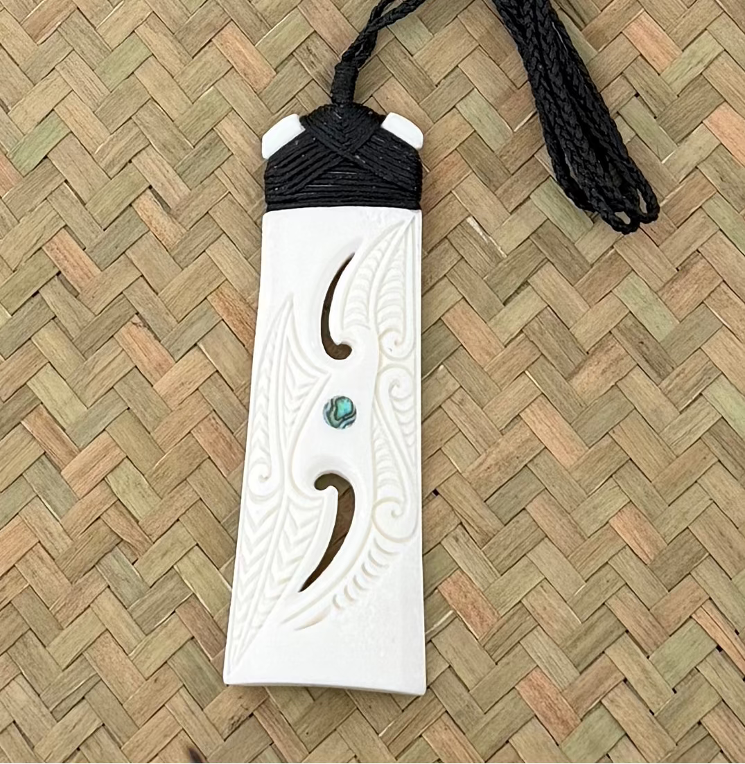 White toki bone carving pendant with black cord on a woven mat