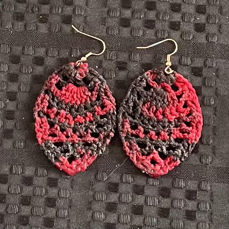 Pair of red and gray crocheted earrings on a textured black surface