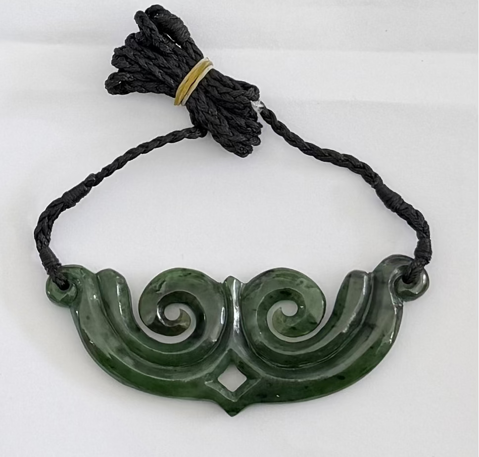 Greenstone pendant on black cord against a white background