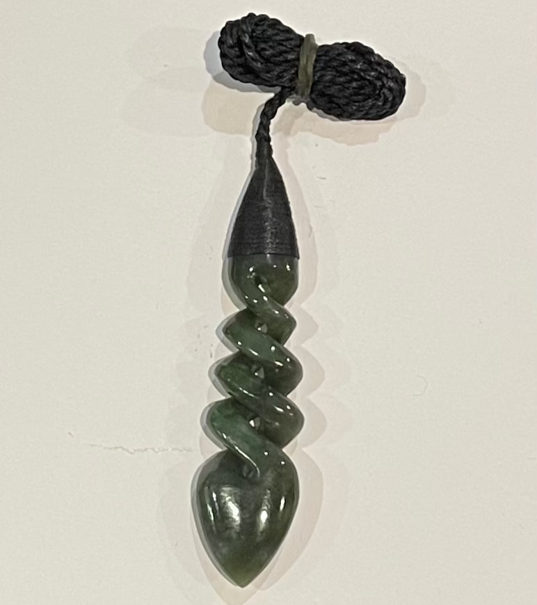 Greenstone Twist necklace pendant on a black cord against a white background