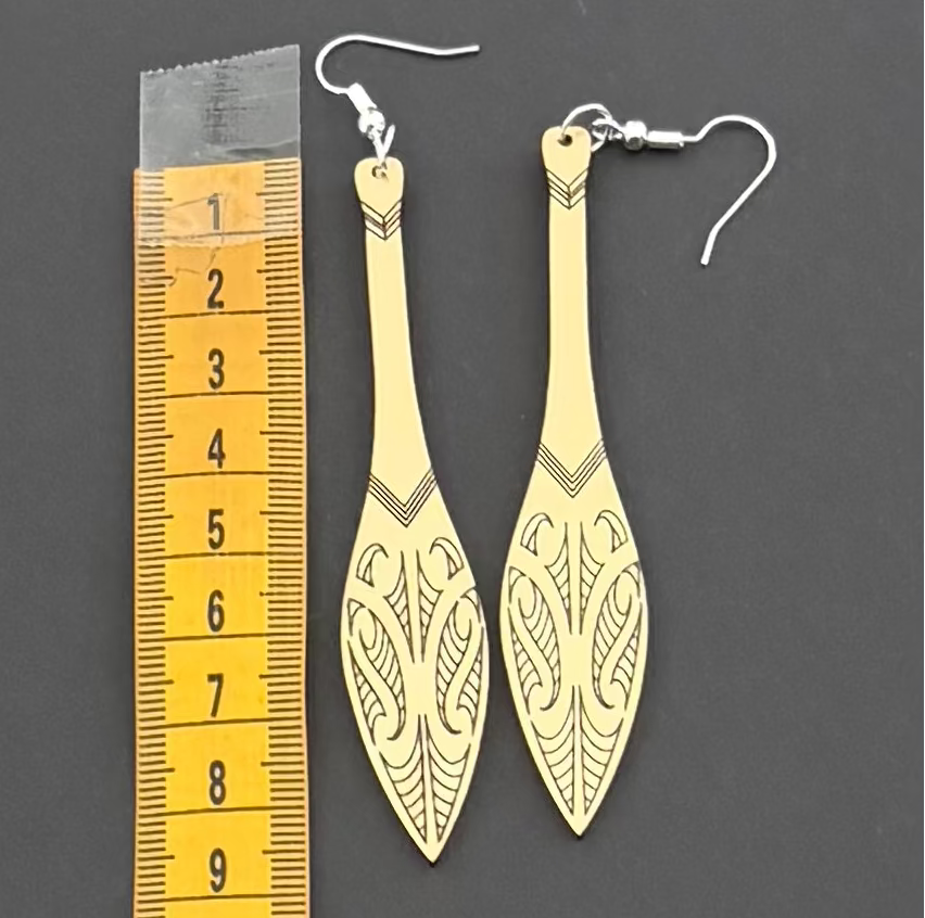 Gold earrings with intricate designs next to a ruler on a dark background