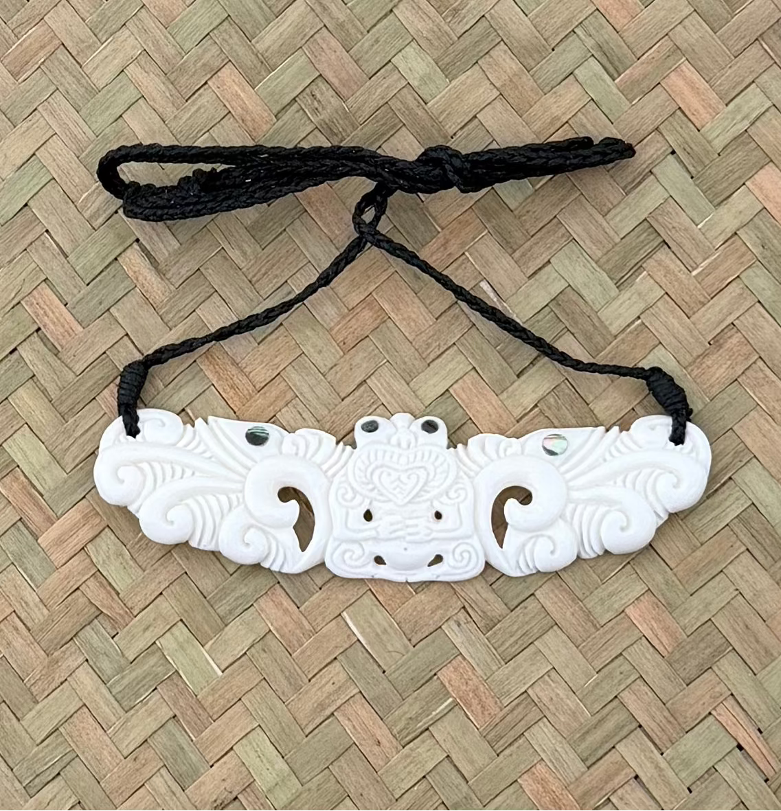 White decorative tiki breastplate bone pendant on a black string against a woven mat background