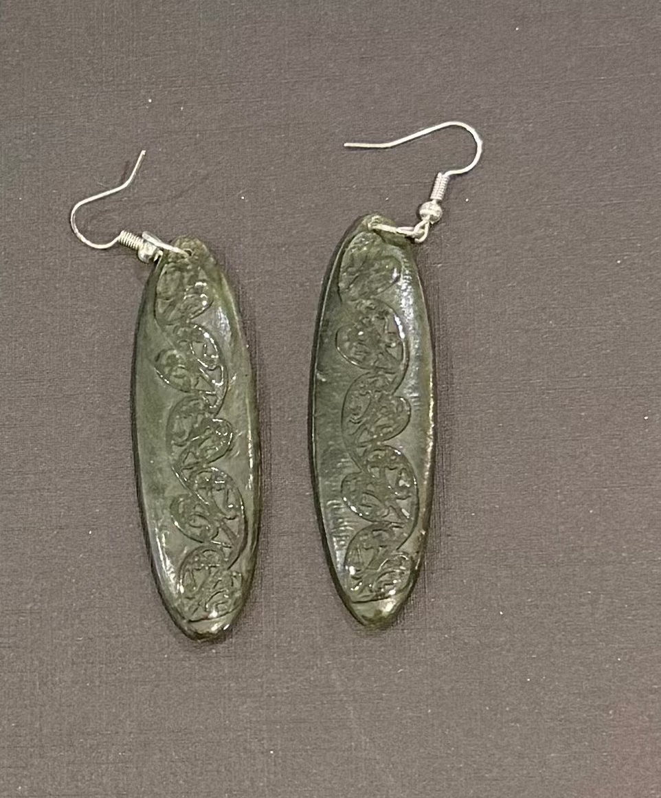Oval-shaped greenstone earrings with intricate designs on a gray background
