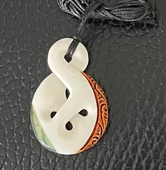 White bone caving pendant with copper detailing on a black leather background
