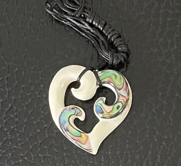 Heart-shaped bone carving pendant with wave design on a black cord against a dark textured background