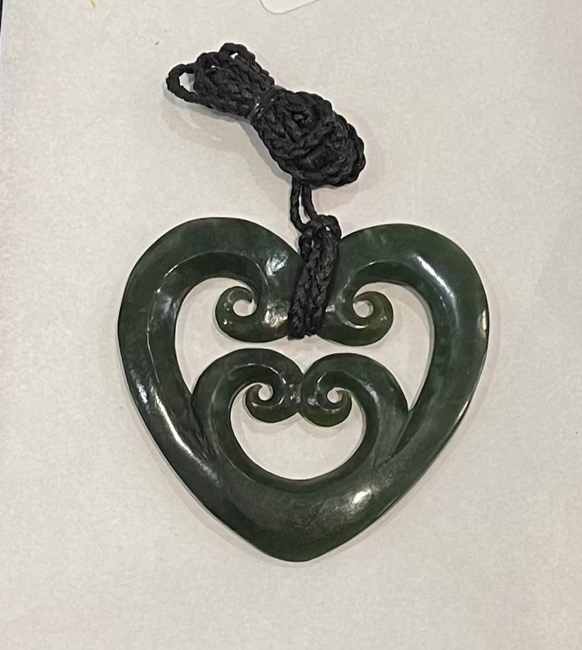 Green jade heart-shaped pounamu necklace with intricate designs on a white background