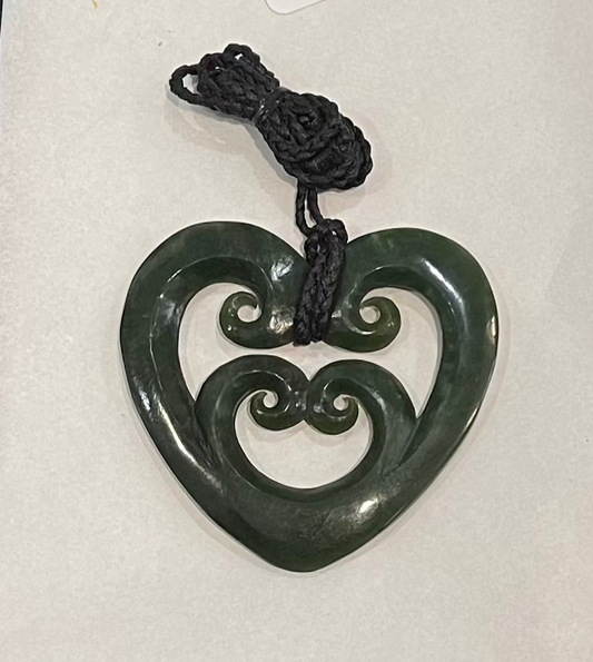 Green jade heart-shaped pounamu necklace with intricate designs on a white background