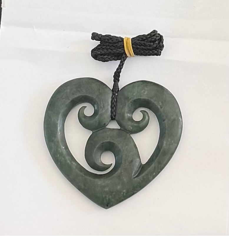 Greenstone heart pendant with intricate design on a white background
