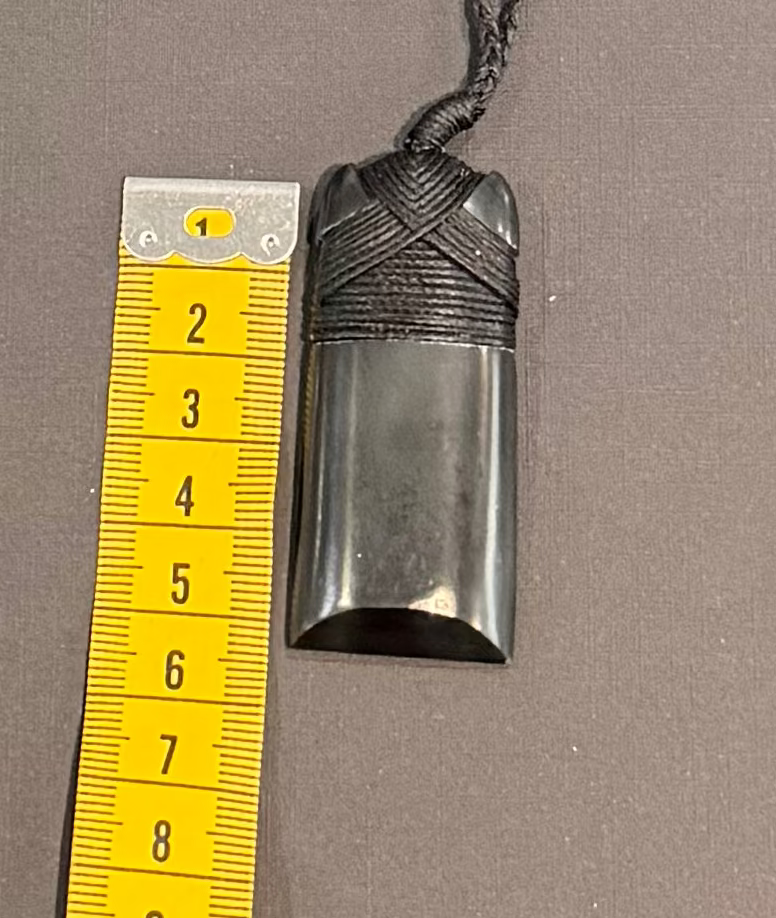 Black pounamu pendant on a string with a yellow measuring tape for scale on a gray background