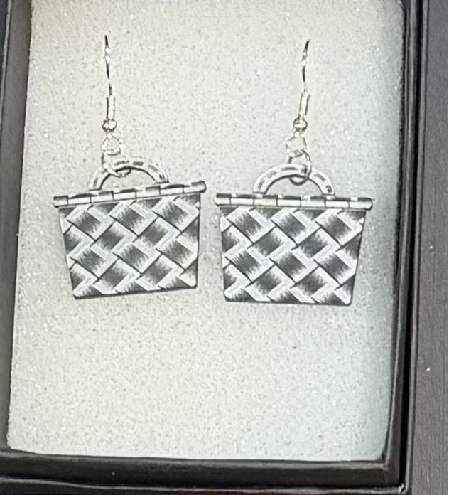A pair of silver dangling earrings shaped like woven baskets, displayed inside a black jewelry box with a light gray insert.