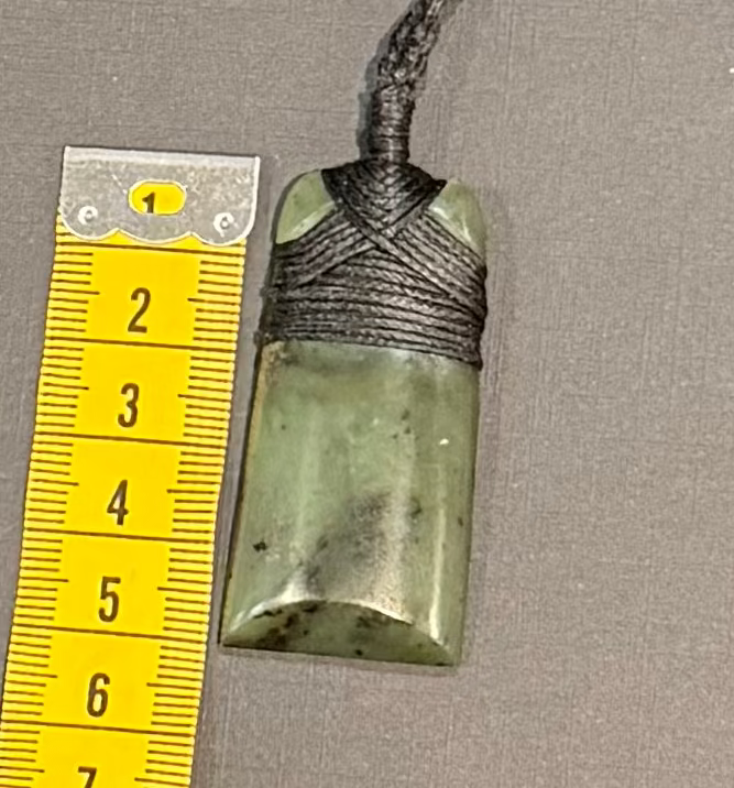Green stone pendant with black cord measurement against a gray background