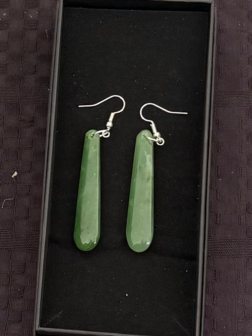 Greenstone earrings in a black display box on a textured black surface