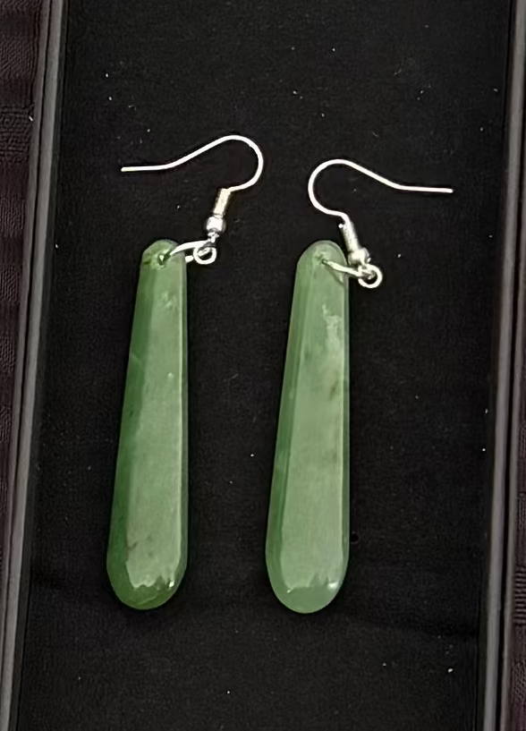 Greenstone earrings in a black display box on a textured black surface