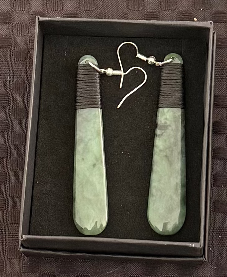 Greenstone earrings in a black box on a textured brown surface