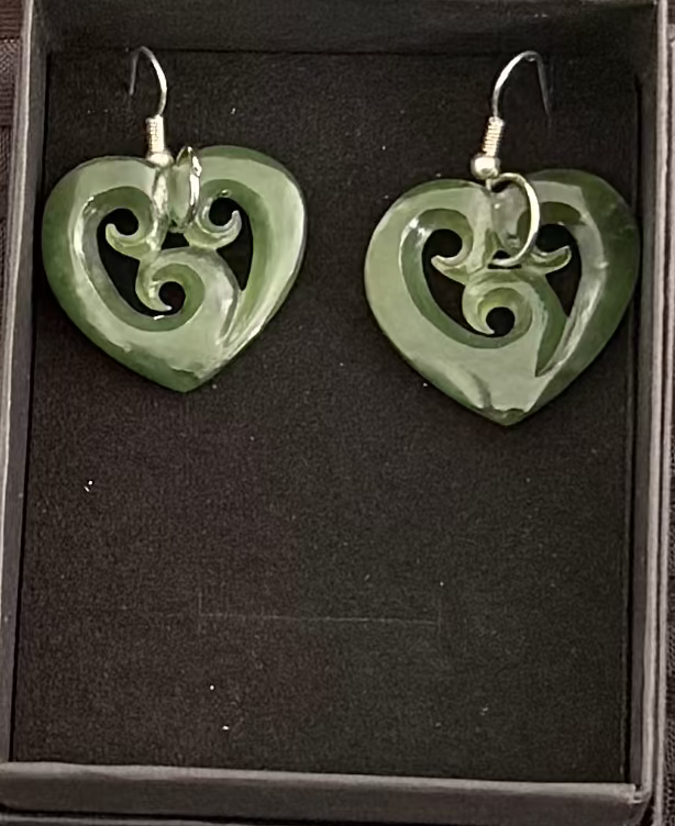 Green heart-shaped earrings in a black box on a textured brown background