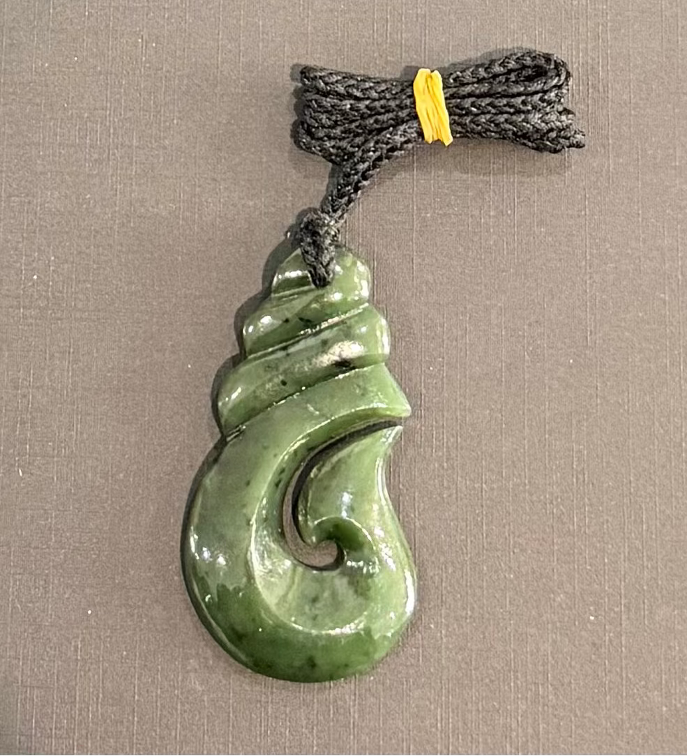 Greenstone hook jade pendant on a brown background