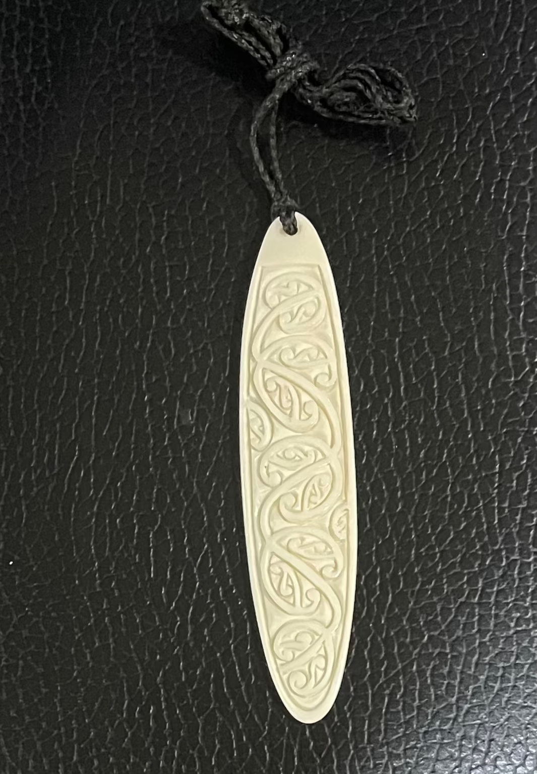 Decorative oval bone pendant on a black leather surface