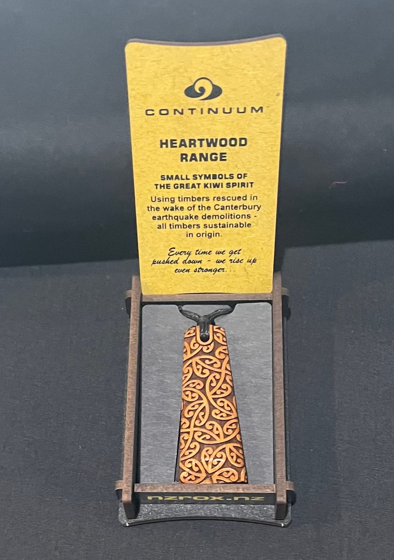 Wooden pendant with 'Continuum' packaging on a dark background