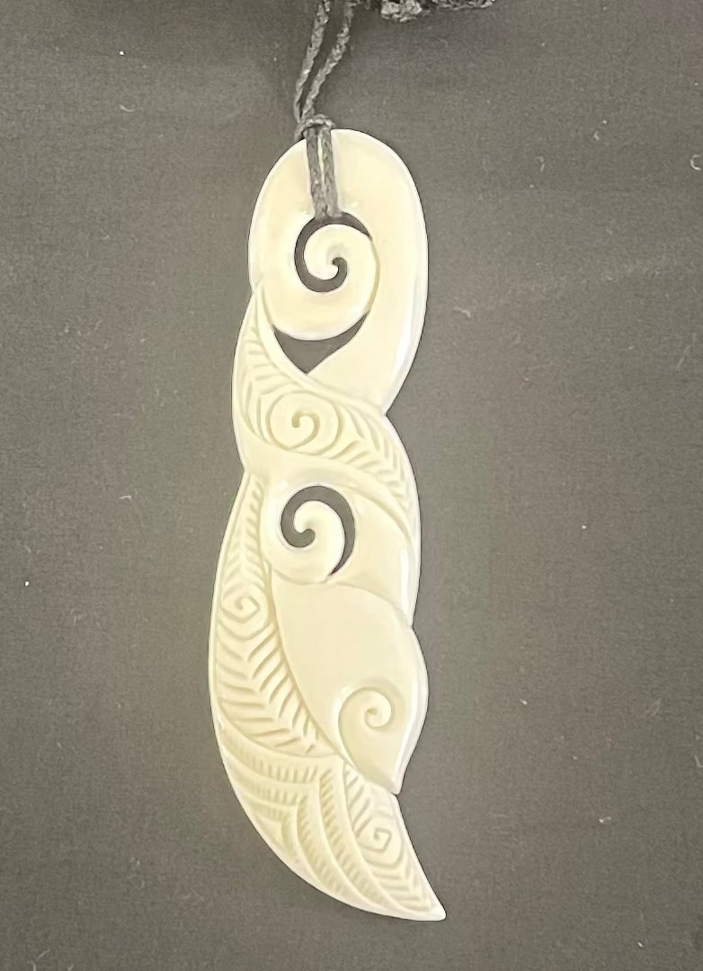 Carved bone pendant with spiral designs on a gray background