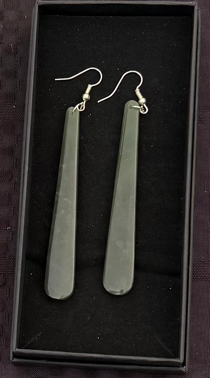 Greenstone earrings in a black box on a textured black background