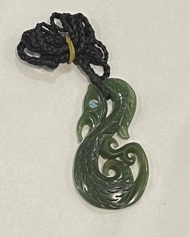Greenstone manaia jade necklace on a black cord against a white background