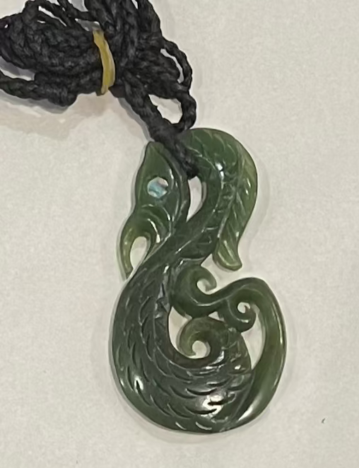 Greenstone manaia jade necklace on a black cord against a white background