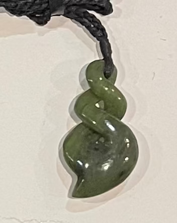 Greenstone spiral necklace pendant on a black cord against a light background
