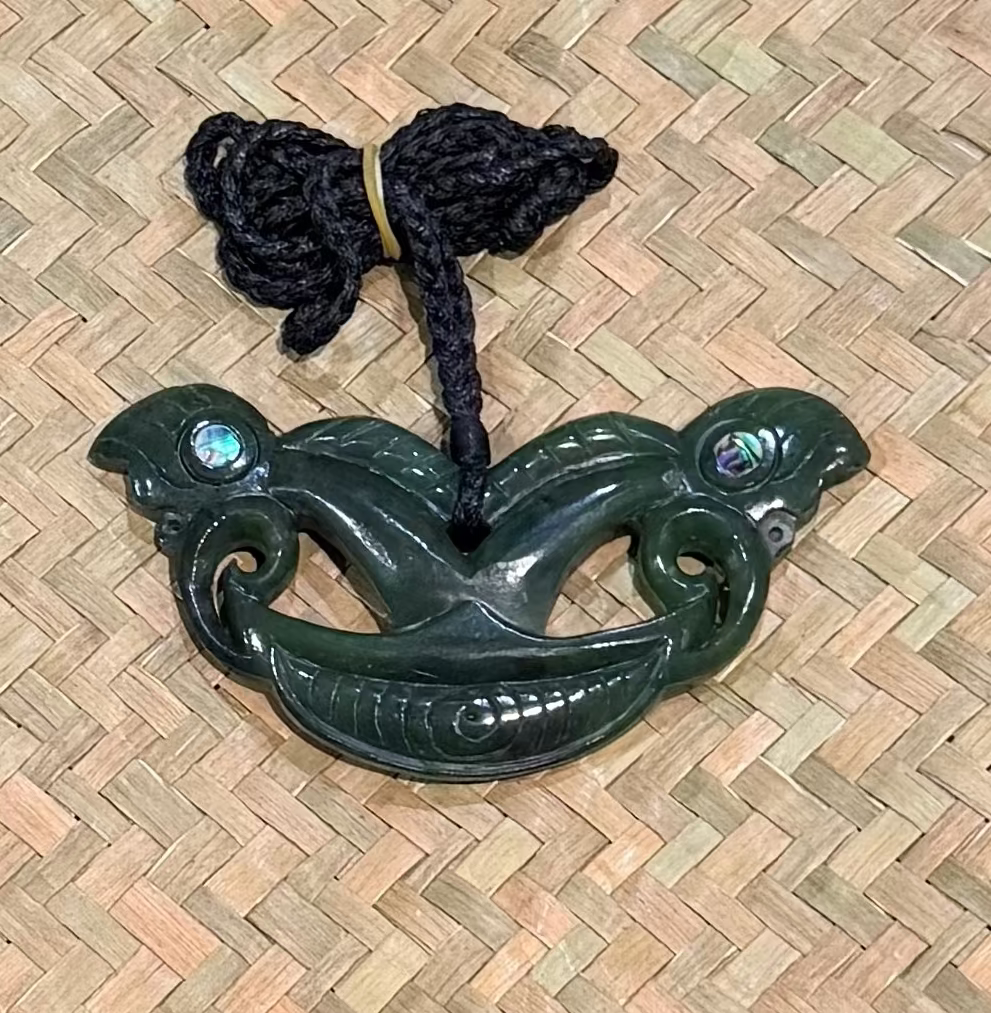 Greenstone jade pendant with black cord on a woven mat