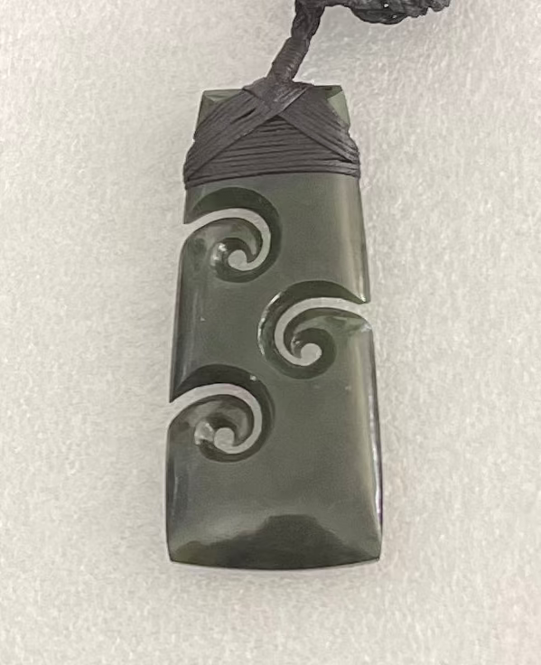 Greenstone pendant with spiral design on a white background