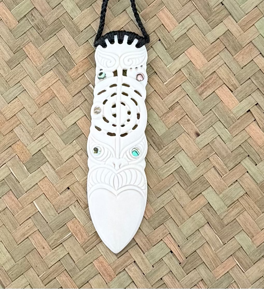 White bone carving decorative item with black cord on a woven mat backgroundE