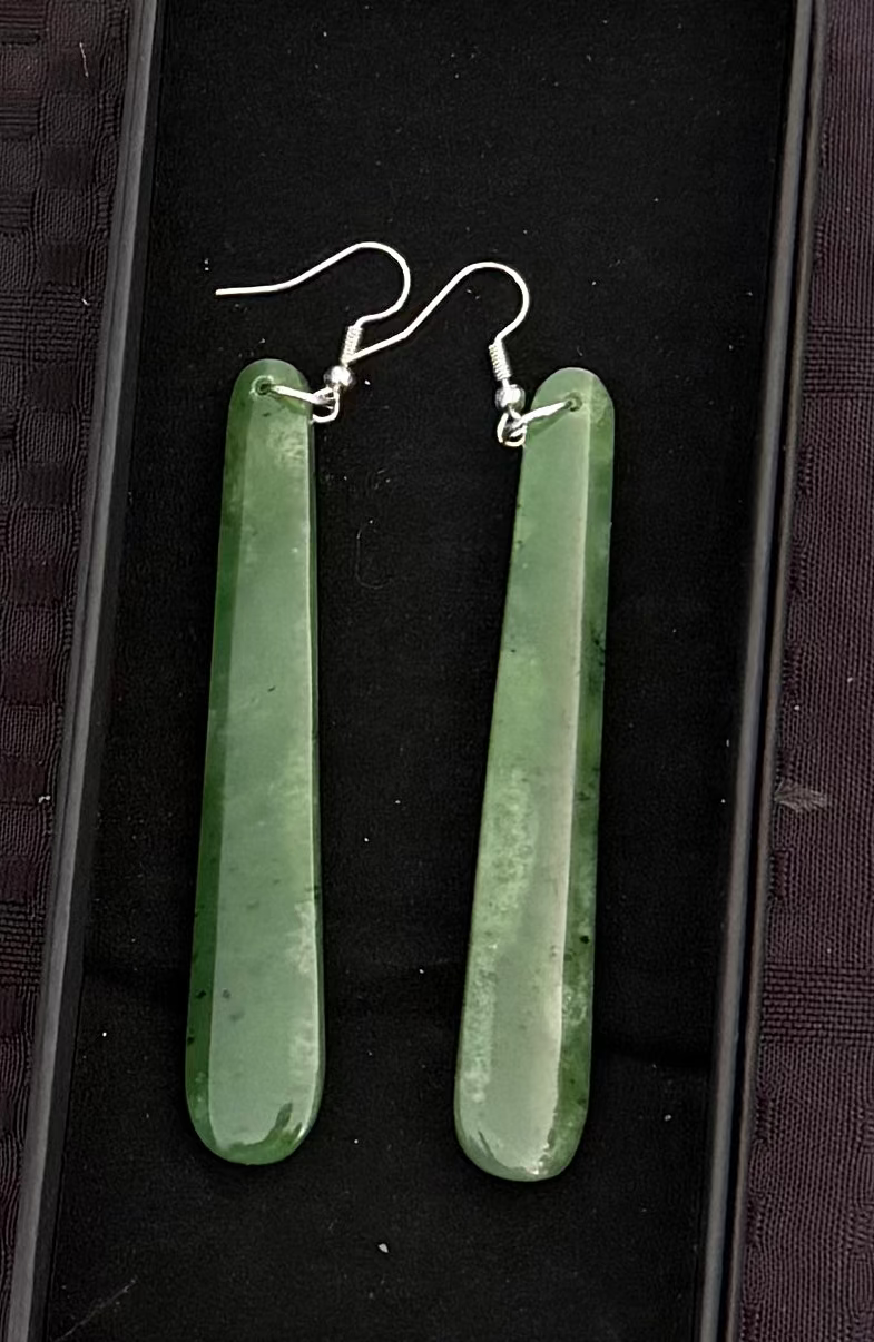 Greenstone-shaped earrings in a black box on a textured black background