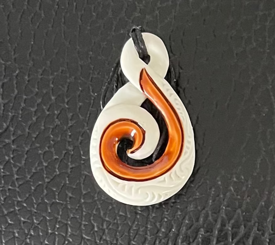 Bone Koru Pendant with a white and brown spiral design on a black textured background