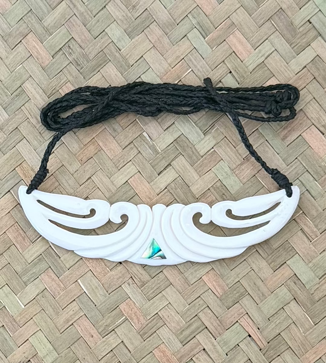 White decorative BONE CARVING with black cord on a woven mat