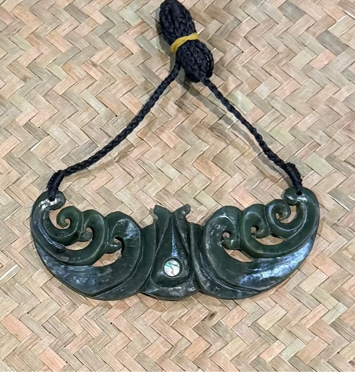 Greenstone pounamu jade necklace with black cord on a woven mat background