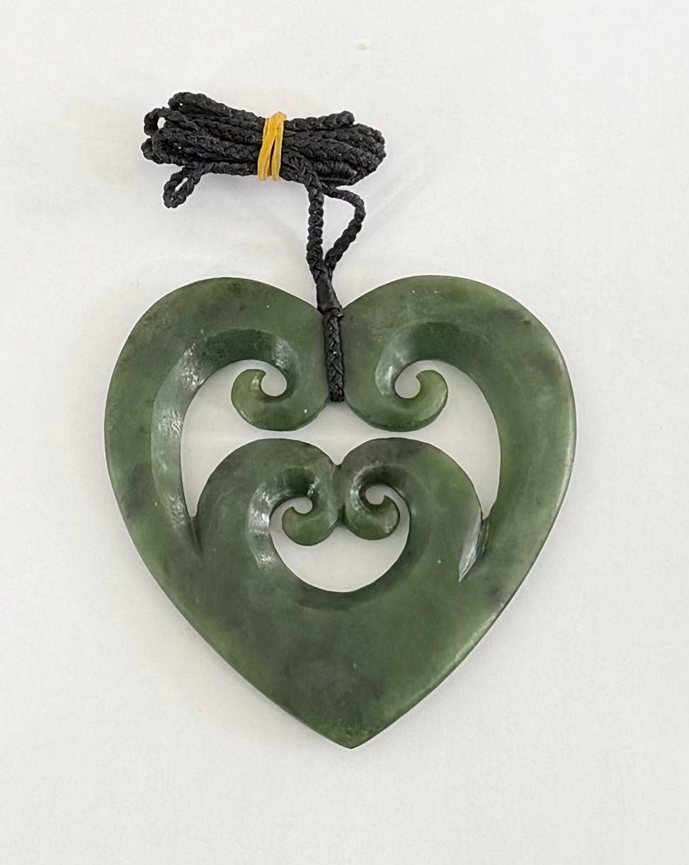 Greenstone jade heart-shaped pendant with spiral design on a white background