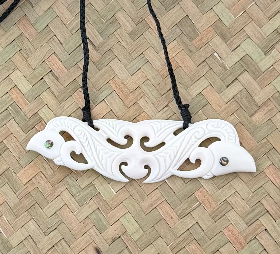 White decorative manaia carved pendant on a black cord against a woven mat background