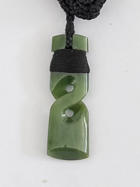 Green jade pendant on a black cord against a white background