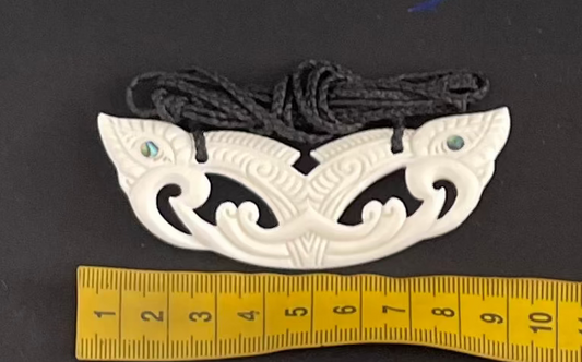 Carved bone pendant with intricate patterns on a black background, measured against a ruler.