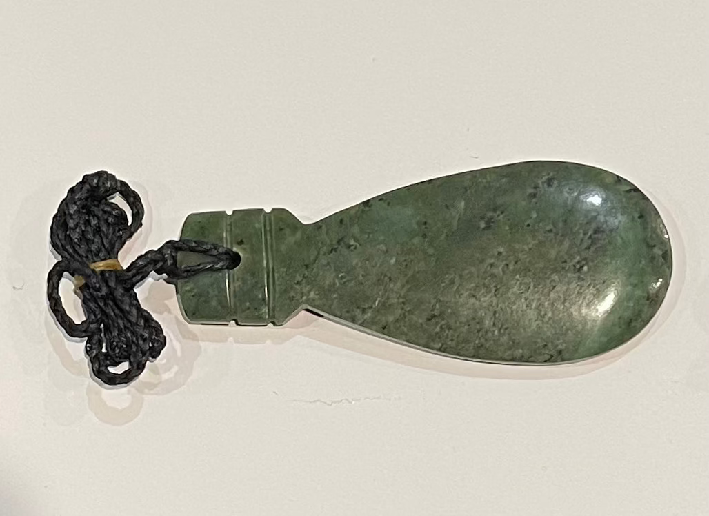 Greenstone patu necklacependant with a black cord on a light gray background