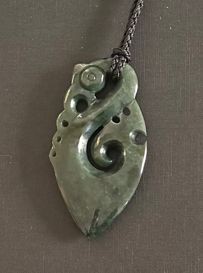 Greenstone manaia jade pendant on a chain against a gray background