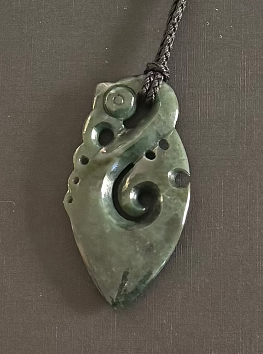 Greenstone manaia jade pendant on a chain against a gray background