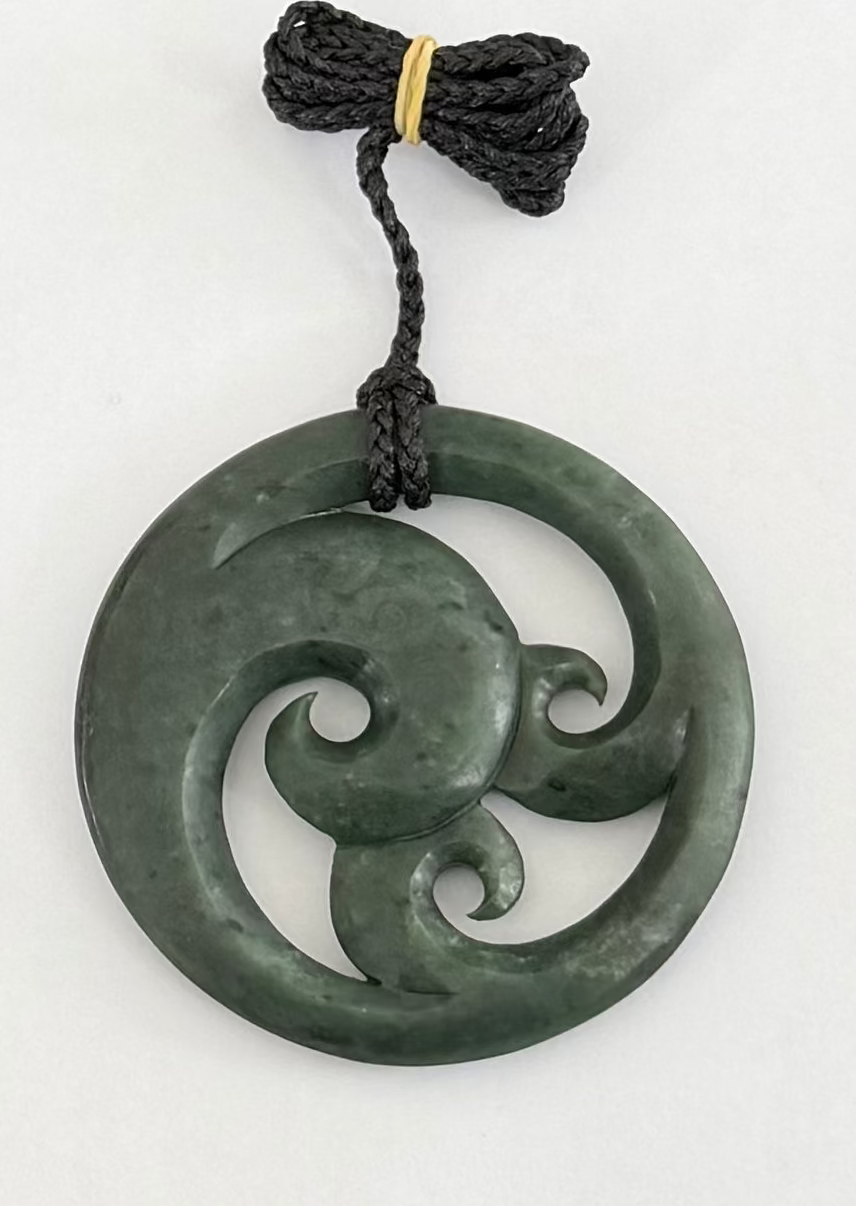 Greenstone circle jade pendant with intricate design on a white background