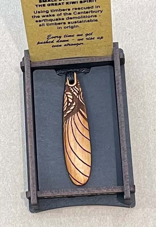 Wooden pendant with feather design on a gray stand with a card above it.