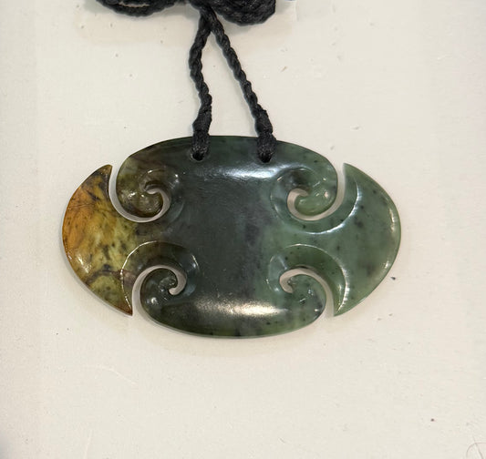 A carved greenstone jade pendant with four spiral cutouts and a black braided cord, photographed on a plain off-white background.