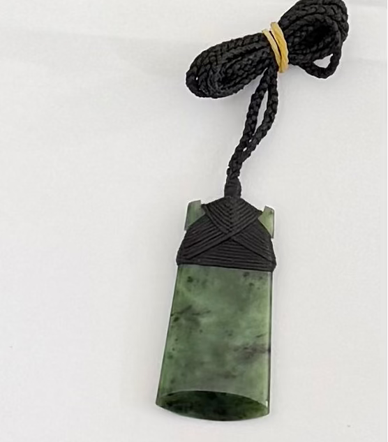 Greenstone toki jade pendant on a black cord against a white background