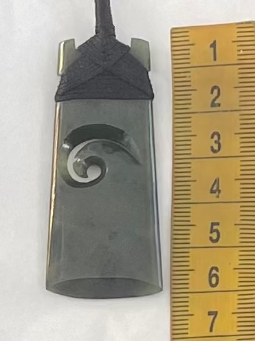 Necklace pendant with wave design next to a ruler on a white background