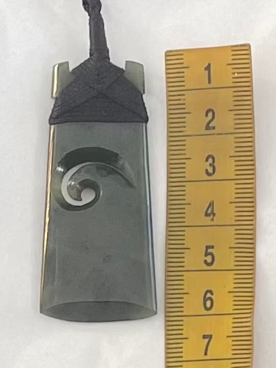 Necklace with a pendant featuring a wave design, next to a ruler for scale on a white background.