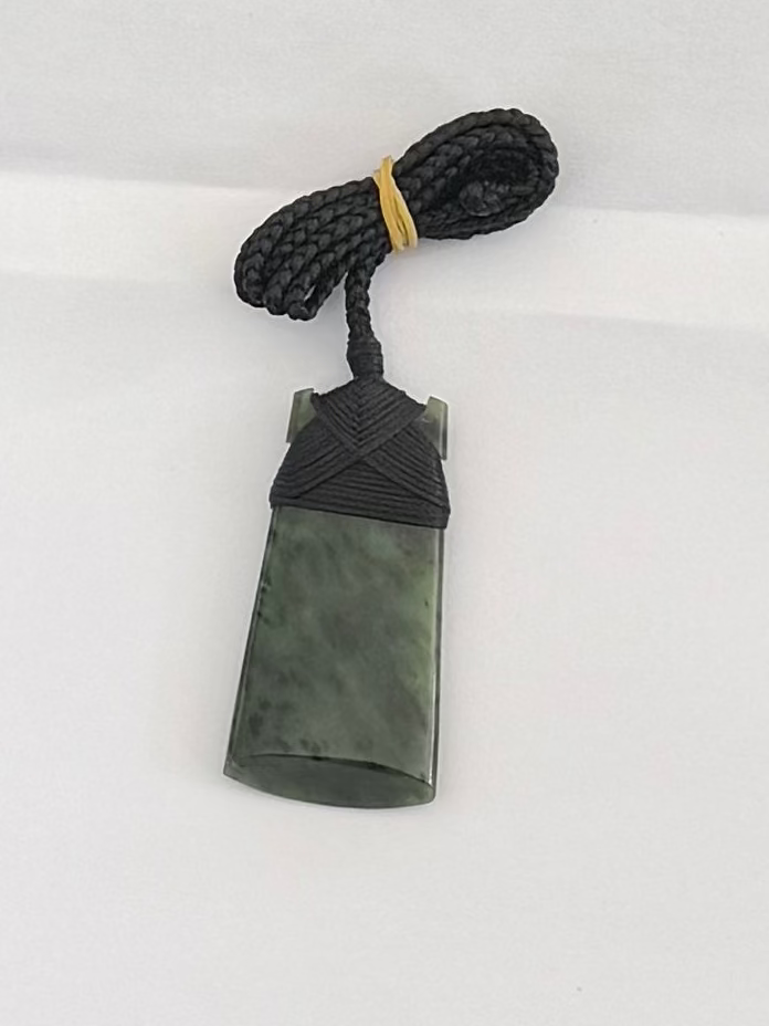 Green stone pendant with black cord on a white background