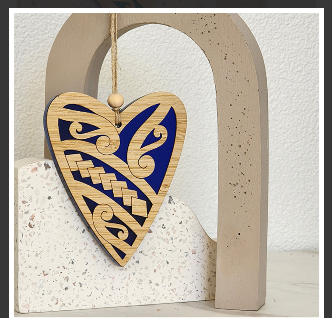 Wooden heart-shaped ornament with blue and gold patterns hanging on a textured wall.