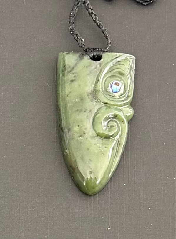 Greenstone jade pendant with spiral design on a gray background